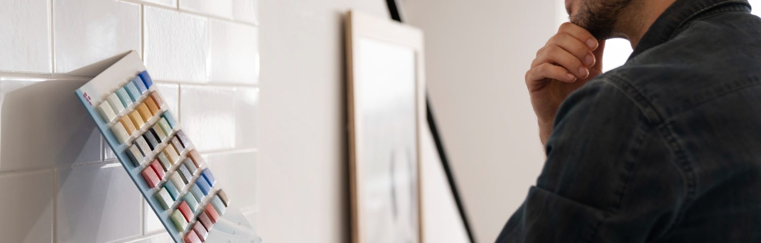 A modern bathroom wall being painted over ceramic tiles with a brush and roller.