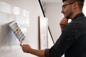 A modern bathroom wall being painted over ceramic tiles with a brush and roller.