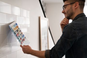 A modern bathroom wall being painted over ceramic tiles with a brush and roller.