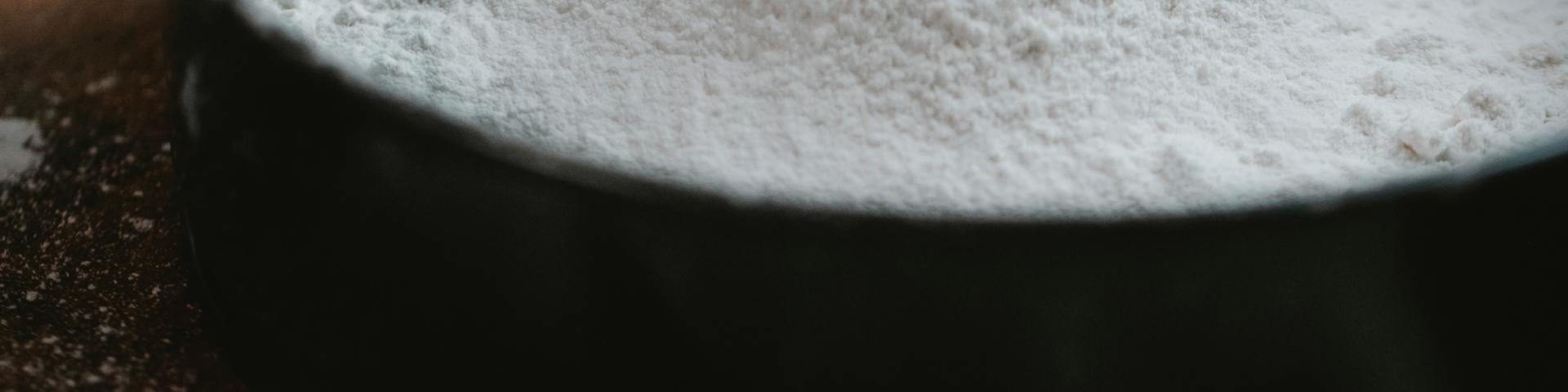 Various types of flour with bread, cakes, and pastries on a wooden kitchen counter.