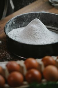 Various types of flour with bread, cakes, and pastries on a wooden kitchen counter.