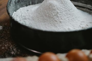 Various types of flour with bread, cakes, and pastries on a wooden kitchen counter.