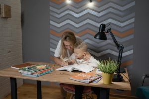 A supportive parent encouraging a primary school child who is concentrating on an open notebook during homework time, illustrating independent learning.